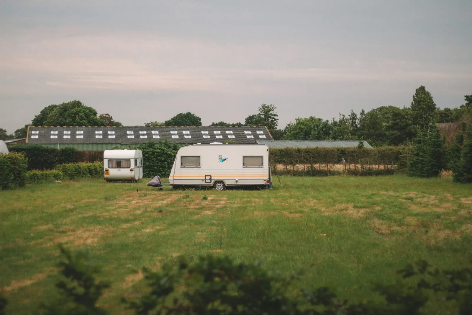 Campingvogne på en grøn plads foran en gård